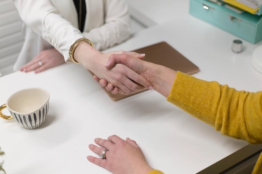 Two people shaking hands across a desk after agreeing a company loan with no personal guarantee